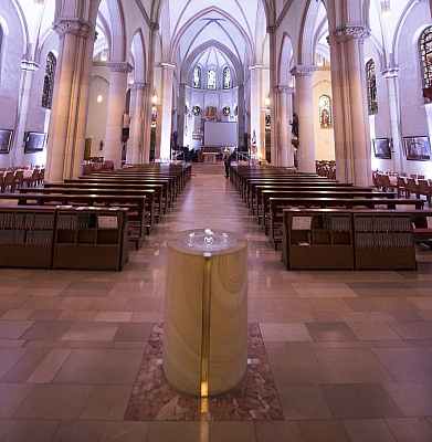 Blick von hinten auf den Taufbrunnen und durch das Mittelschiff der violett beleuchteten St. Agatha-Kirche Blick von hinten auf den Taufbrunnen und durch das Mittelschiff der violett beleuchteten St. Agatha-Kirche