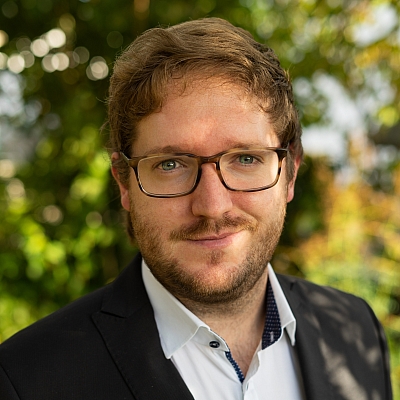 Portraitaufnahme von Artur Jurczyk in Anzug. Im Hintergrund ist grüne Natur.