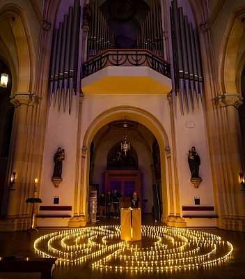 Blick von der Seite auf das Labyrinth aus Teelichtern und den Taufbrunnen. Oberhalb hängen Orgelpfeifen. Blick von der Seite auf das Labyrinth aus Teelichtern und den Taufbrunnen. Oberhalb hängen Orgelpfeifen