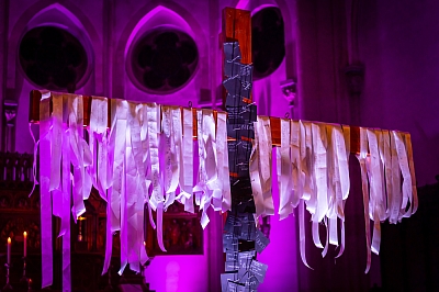 An einem Holzkreuz sind weiße Bänder und schwarze Zettel angeheftet. Die Kirche ist stimmungsvoll beleuchtet. An einem Holzkreuz sind weiße Bänder und schwarze Zettel angeheftet. Die Kirche ist stimmungsvoll beleuchtet.