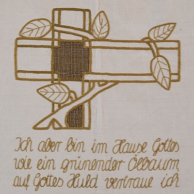 Gesticktes Bild im Hungertuch: Das Bild zeigt uns einen Ölbaum, der sich um das Kreuz Christi legt, ihn kleidet und sich selbst stützen lässt durch das Kreuz.