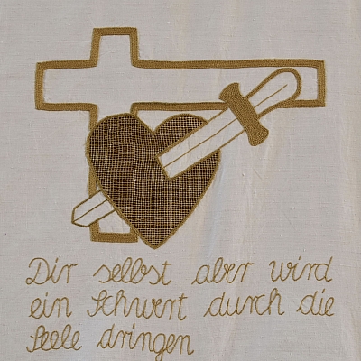 Gesticktes Bild im Hungertuch: Ein Herz wird von einem Schwert durchstoßen. Im Hintergrund ein Kreuz. Darunter ein Bibelvers und die Namen der Stickerinnen.