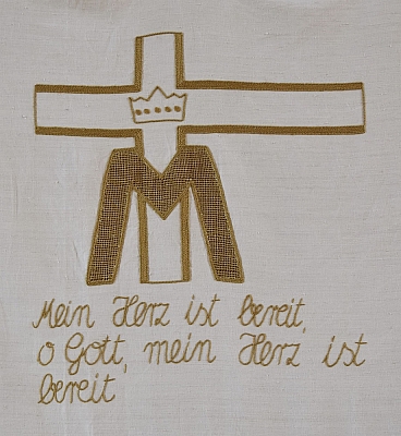 Gesticktes Bild im Hungertuch: Ein großes M für Maria und darüber eine Krone. Dahinter das Kreuz. Gesticktes Bild im Hungertuch: Ein großes M für Maria und darüber eine Krone. Dahinter das Kreuz.